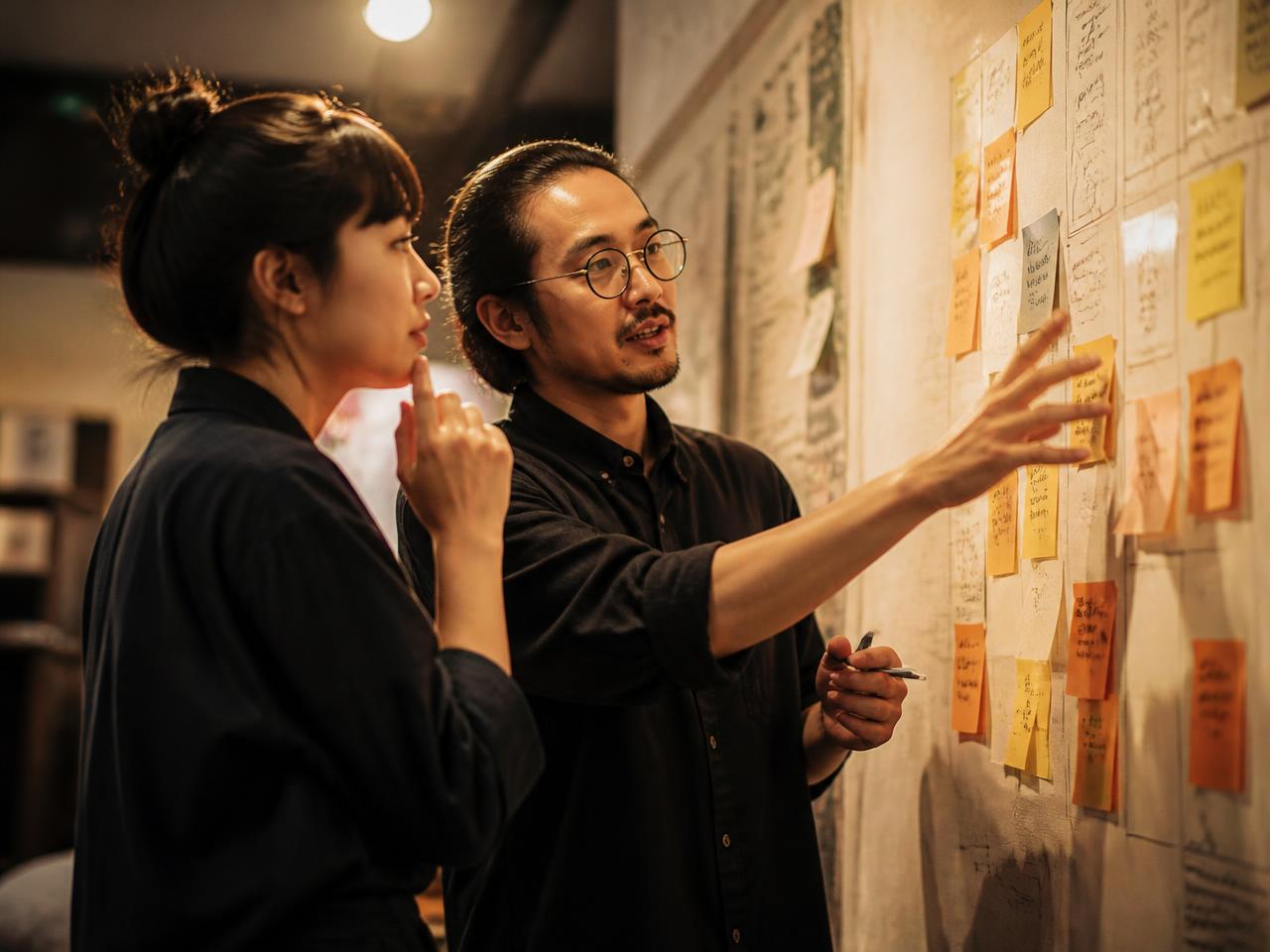 Two strategists mapping a plan on a wall of notes